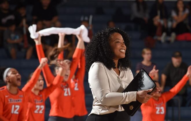 an african american woman smiling in a gym with woman volleyball players