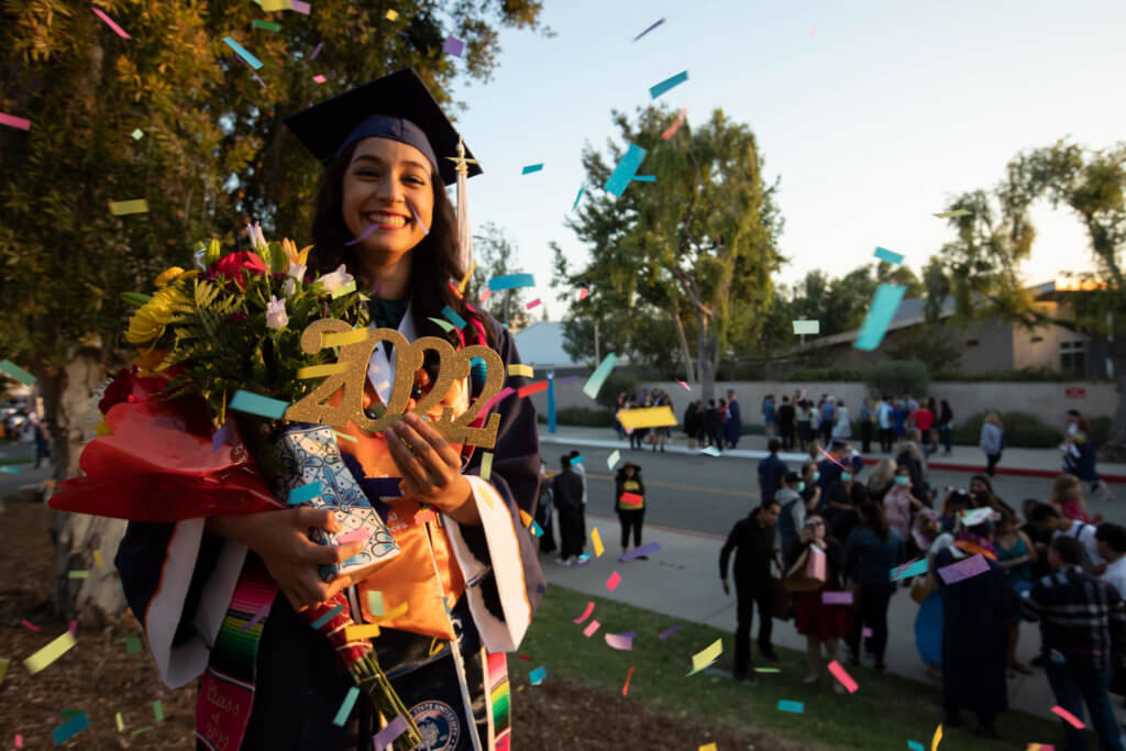 Graduate holding "2022" sign and flowers, smiling. 