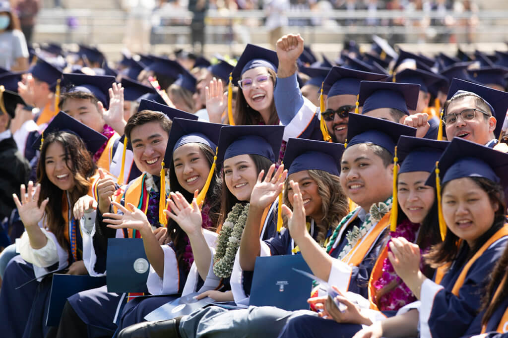 Group of seated graduates wave to the camera