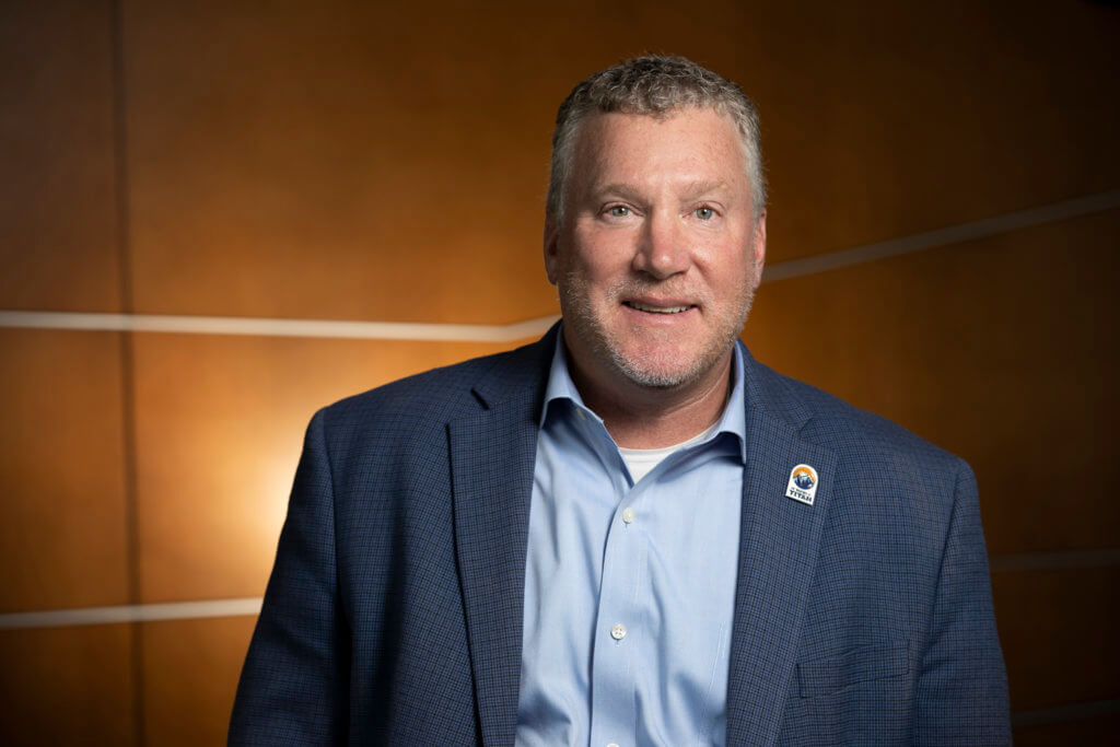 man in a suit jacket, blue shirt and smiling