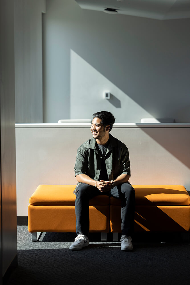 Jovin Justice Adamos sits on an orange bench in housing.