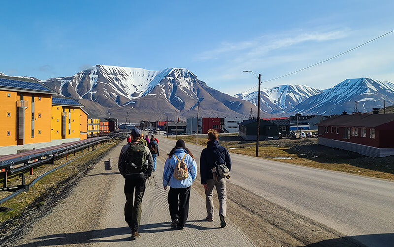 A group of college students walk down a road toward snow-capped mountains in Svalbard.