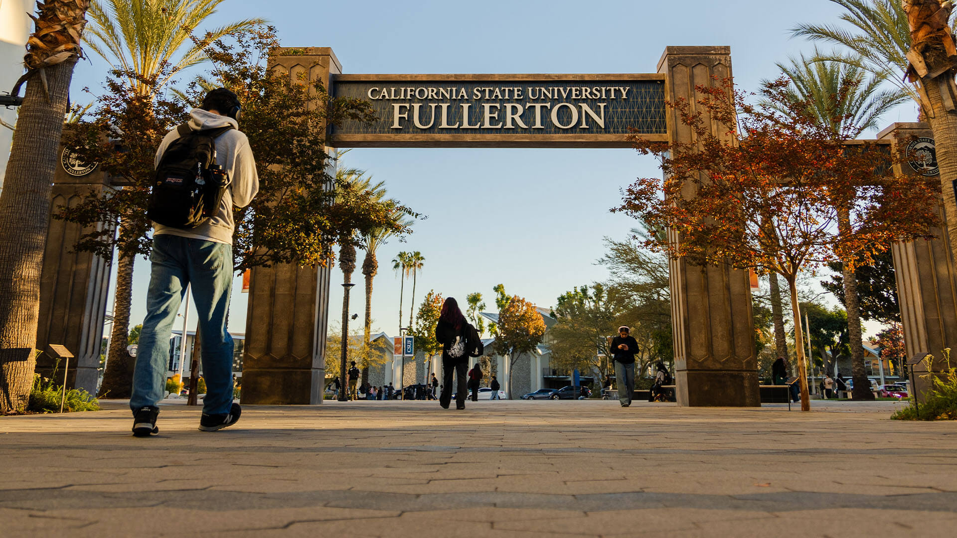 Students walk under the California State University Fullerton entrance arch on a sunny day.