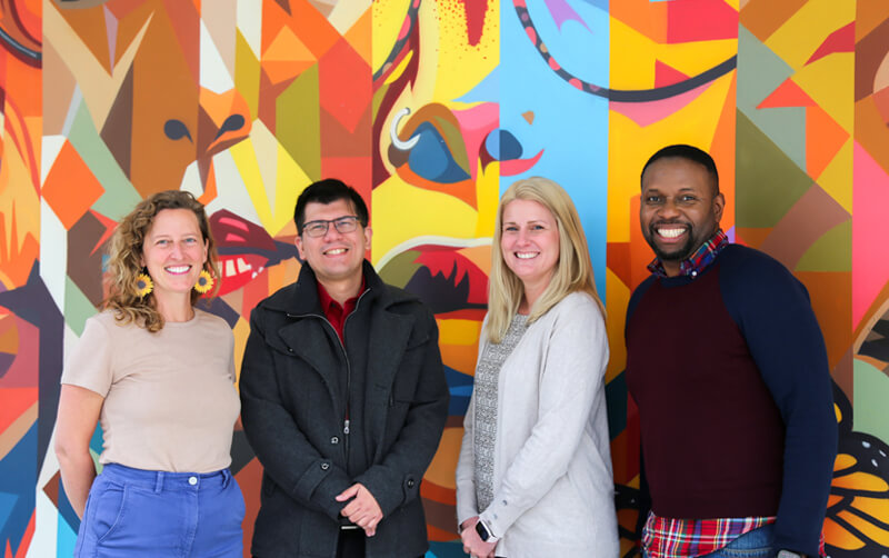 Group of professors in front of mural who are collaborating on AI literacy project