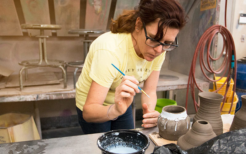 Student working to glaze a pot.