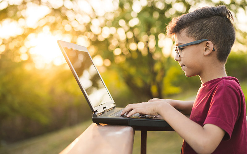 Young boy attends CSUF Summer Youth camp virtually on a laptop.