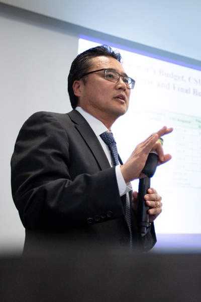 Dark-haired man with glasses gives a powerpoint presentation on the university budget.