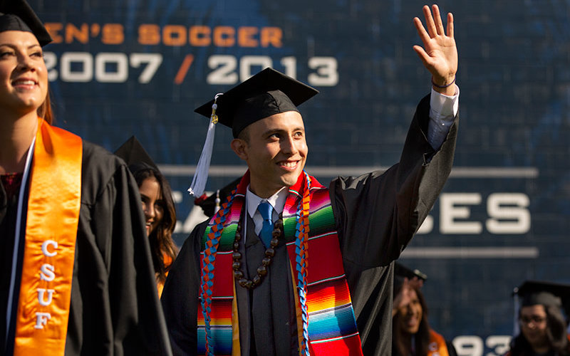 Hispanic graduate waving at commencement.