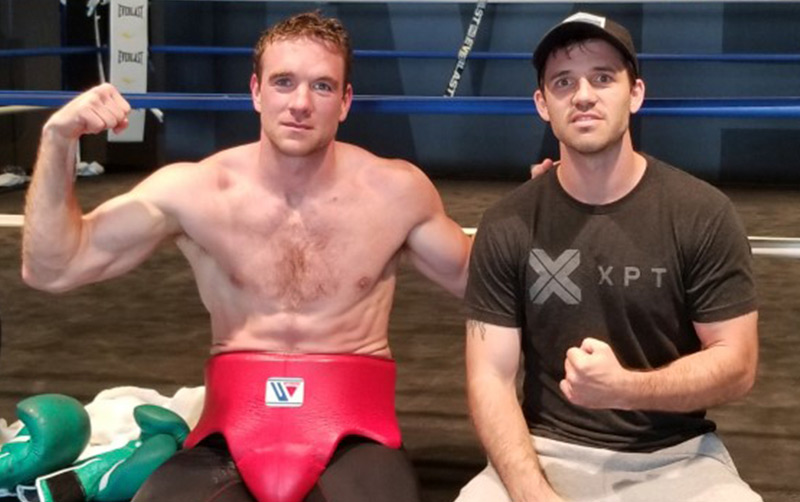 Mike Lee and Andy Galpin flex in a gym.