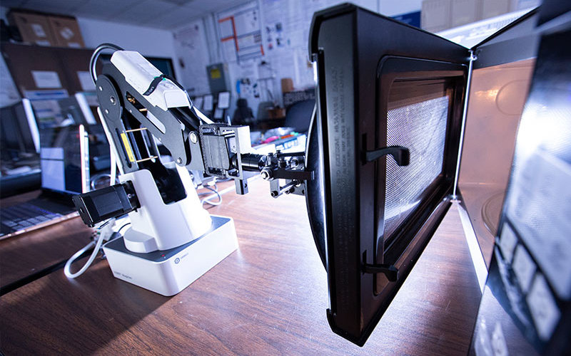 Robotic arm opens a microwave oven.