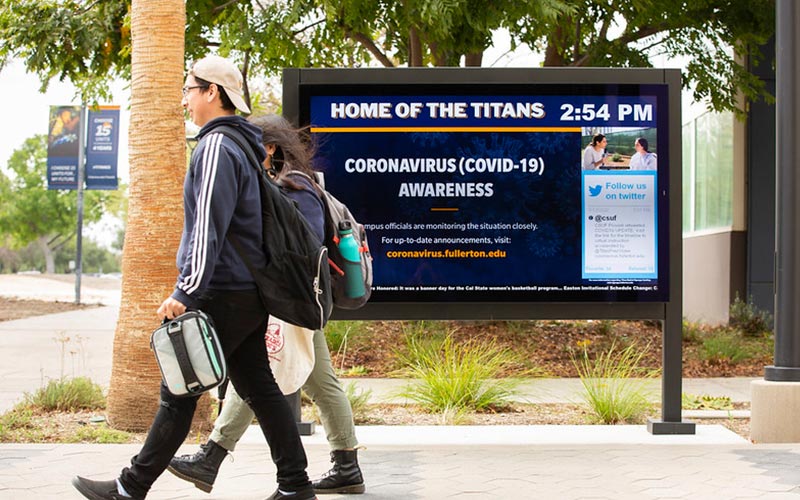 Students walk in front of digital signs with displaying COVID-19 information