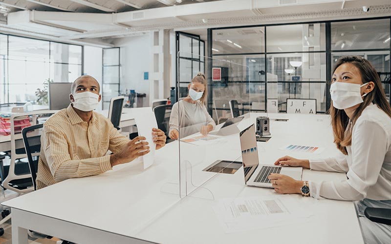 People wearing masks working in an office with glass partition dividing them