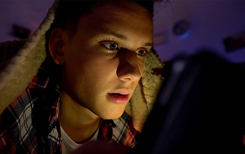 Teenager lying under blanket and using tablet
