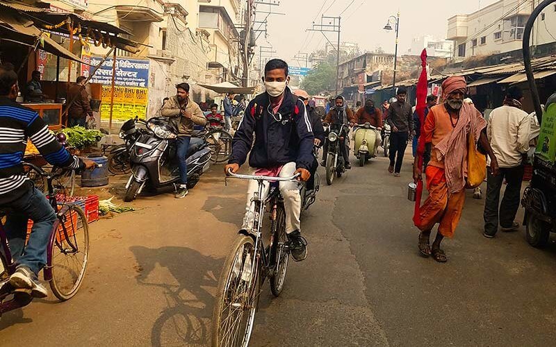 An idividual with a mask rides a bike through an Indian street with air pollution.