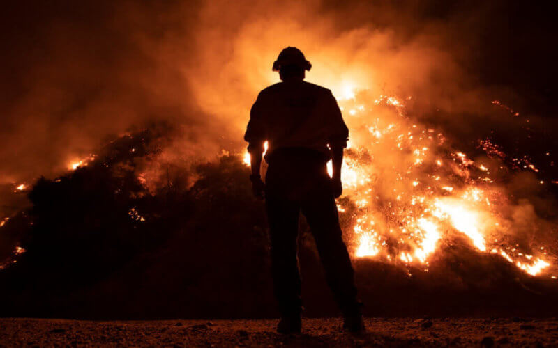 Firefighter stands in front of burning hillside at night