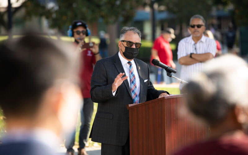 man at a lectern wearing a mask outdoors