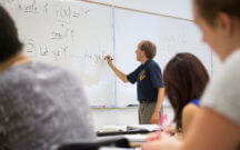 Teacher at white board writing math equation