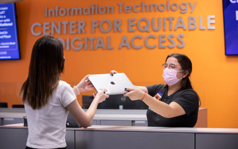 A Student Assistant at the Center for Equitable Digital Access hands out a laptop for a student.