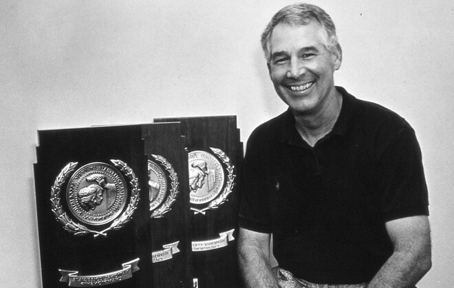 man wearing a polo shirt smiling with three trophies