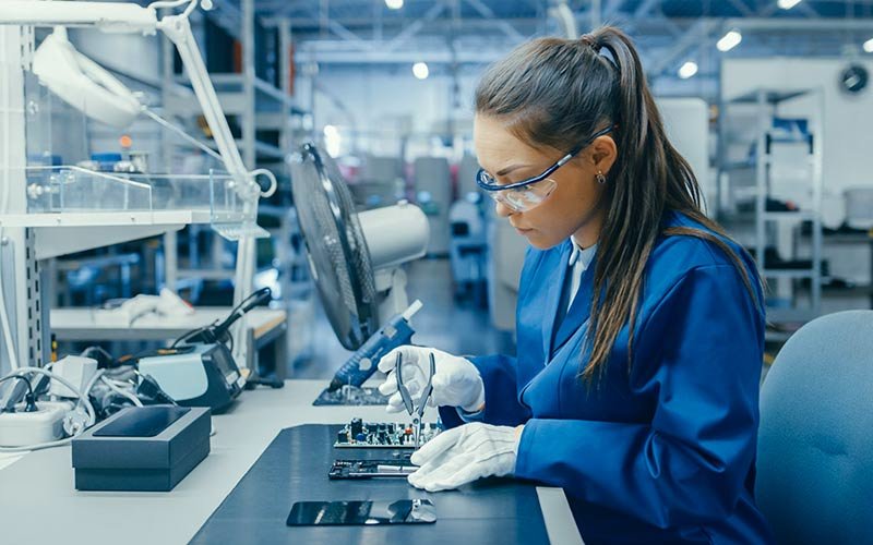 Female engineer wearing a blue lab coat, goggles and white gloves in a manufacturing plant working on a project