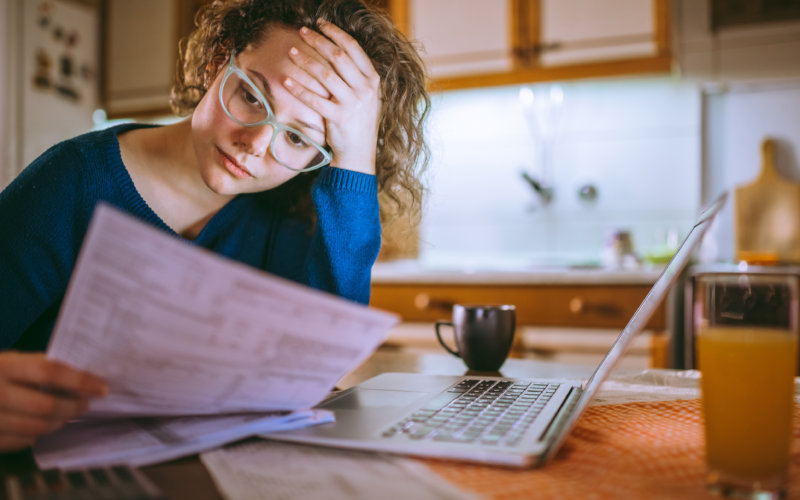 Young female reading documents, using laptop in the kitchen at home