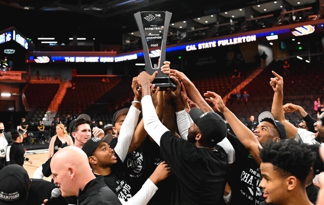 men wearing black t-shirts and caps inside a gymnasium holding up a trophy