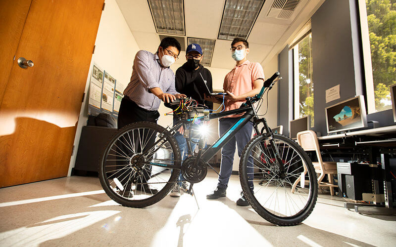 Professor Yu Bai works with students Ivan Rodriguez and Ryan Luong on their AI bicycle.