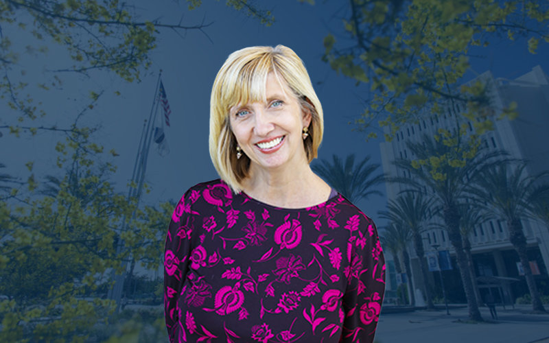 Professional female headshot with blonde hair, earrings, and a black and pink top in front of a CSUF backdrop