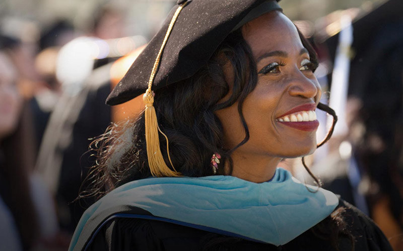 Black female wearing CSUF cap and gown smiling with pride