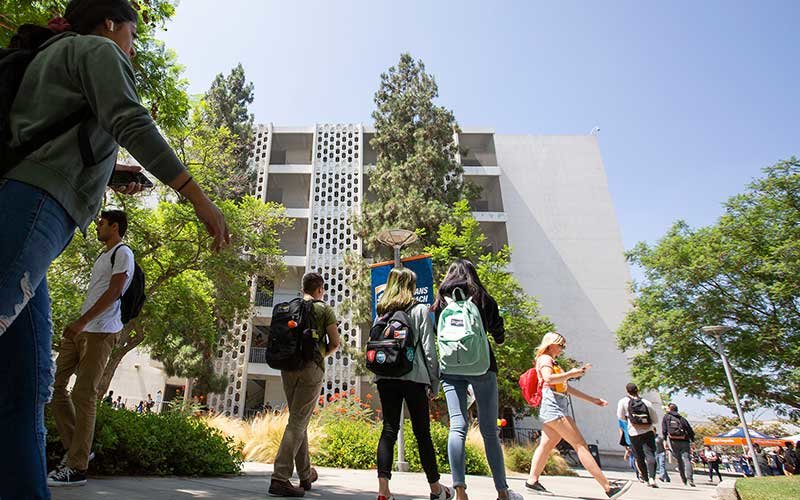 Diverse CSUF students, wearing backpacks, walking on campus