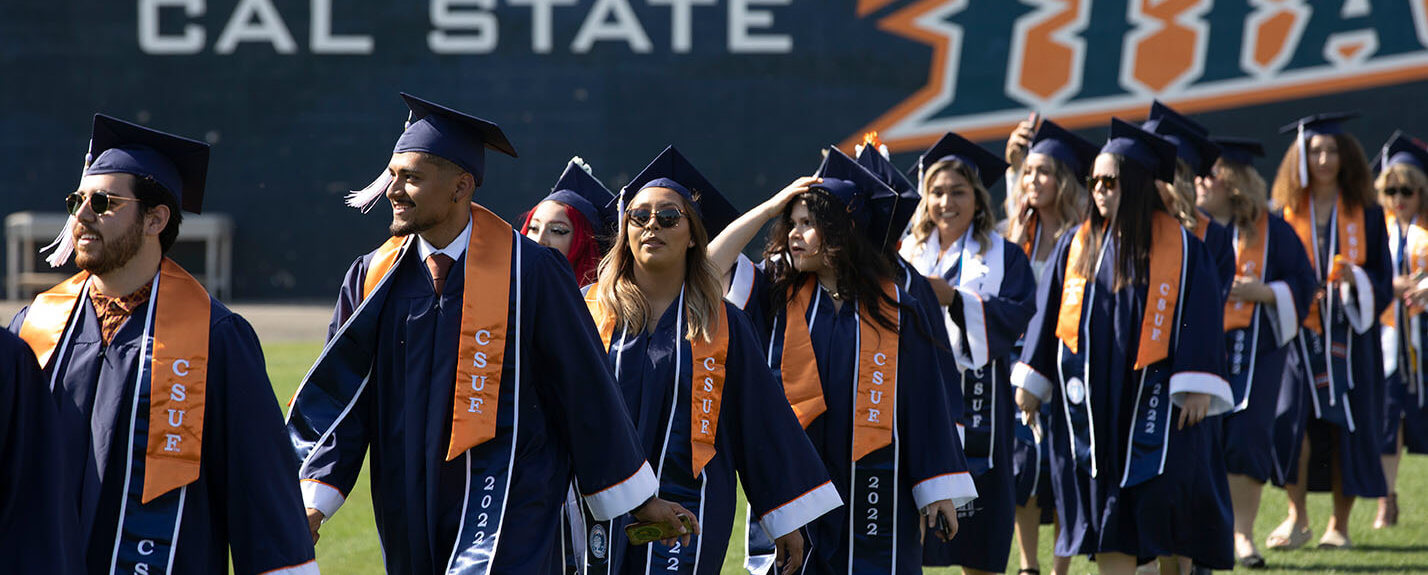 Graduates walk across field in regalia