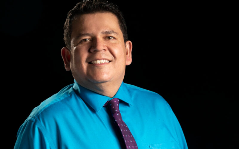 a man wearing a teal shirt and black tie smiling