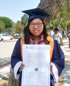Joann Lam poses in Commencement regalia with diploma