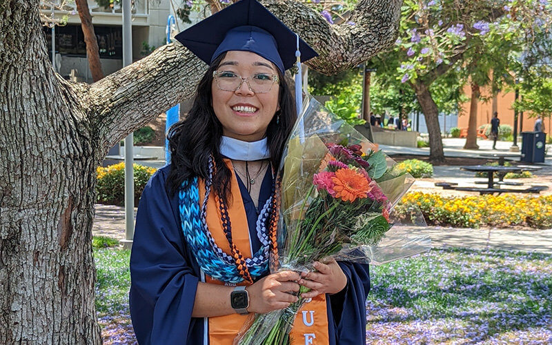 Michelle Okawa posing with flowers in commencement regalia