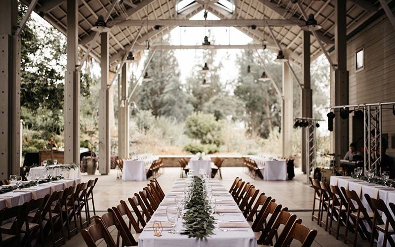 Picturesque view of an event set up under Bacon Pavilion at Fullerton Arboretum with trees and plants in the background and tables and chairs set up for a planned event