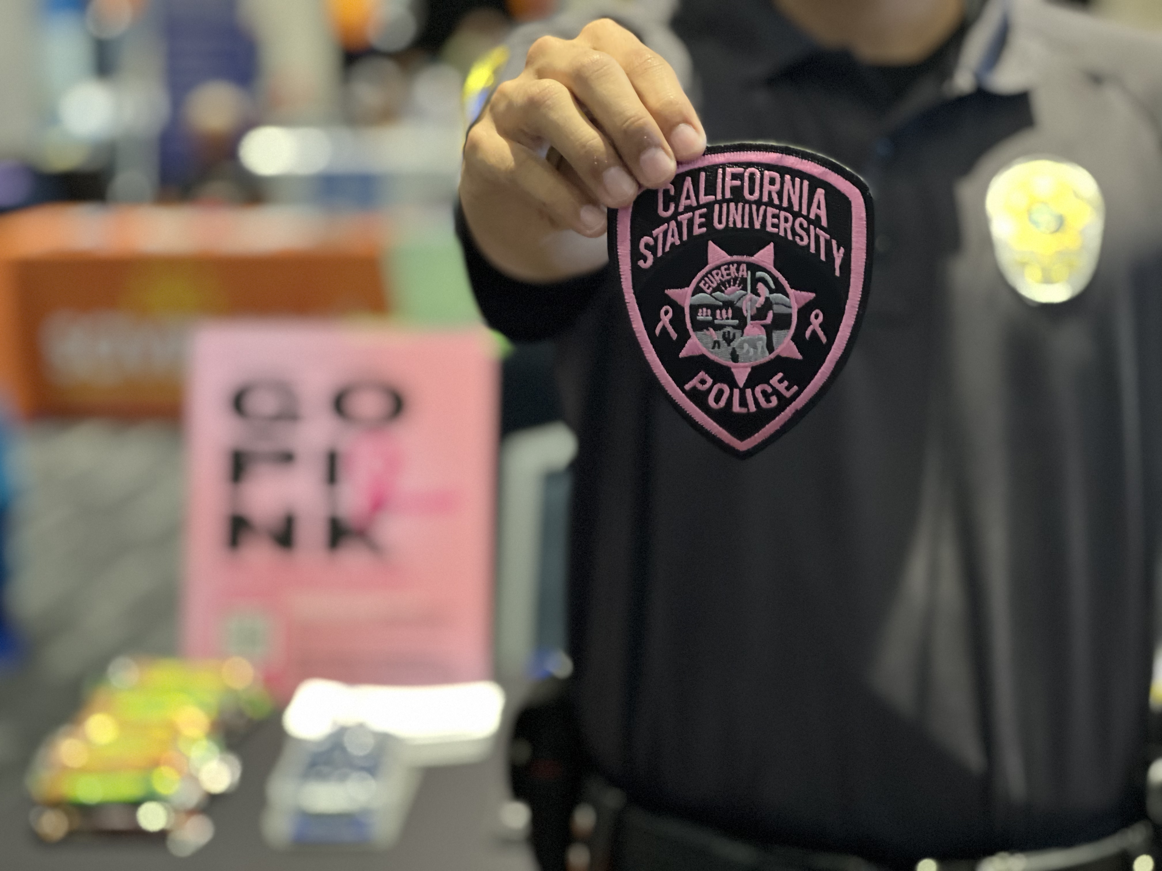 A CSUF PD student employee holding a pink and black breast cancer awareness police patch.