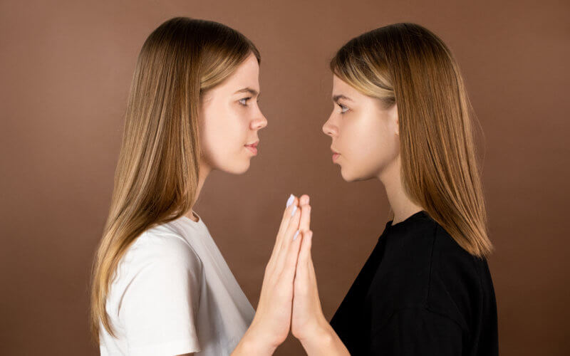 Side view of twin teenage girls touching by hands and looking at one another