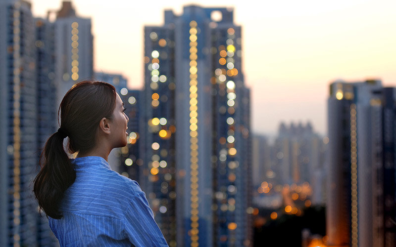 Young woman with her hair pulled back, wearing a blue blouse, looking out yonder at the city lights