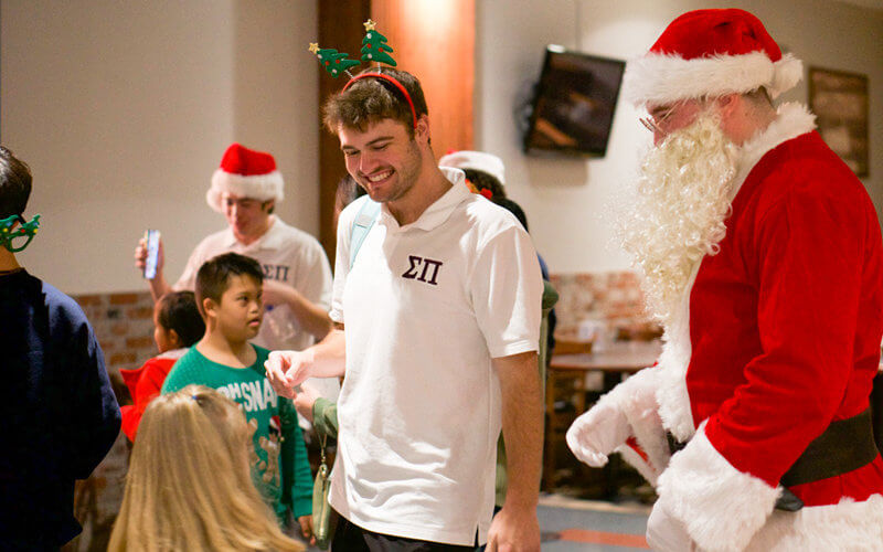 Sigma Pi fraternity members Nolan Winter and Alec Lewis (aka Santa) welcome children to the holiday party at Titan Student Union.