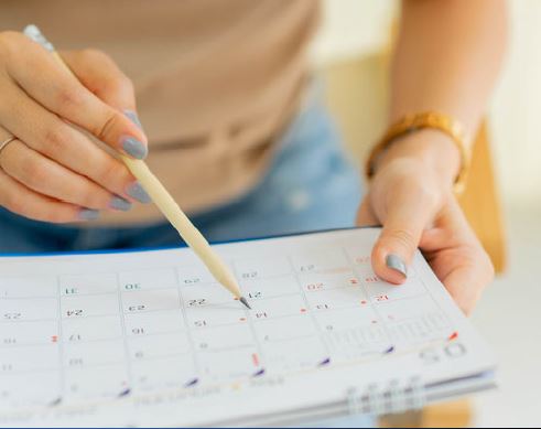 A person is holding a pencil, and they are writing on a paper calendar