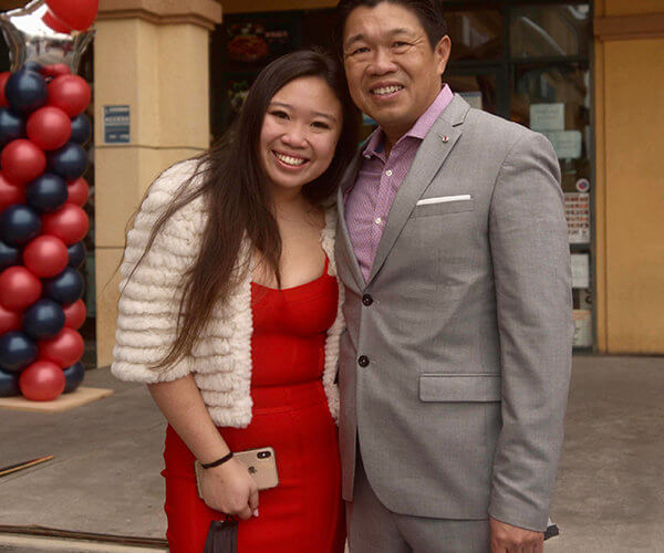 Alumna Vivian Yenson with father at restaurant opening wearing red dress and white coat