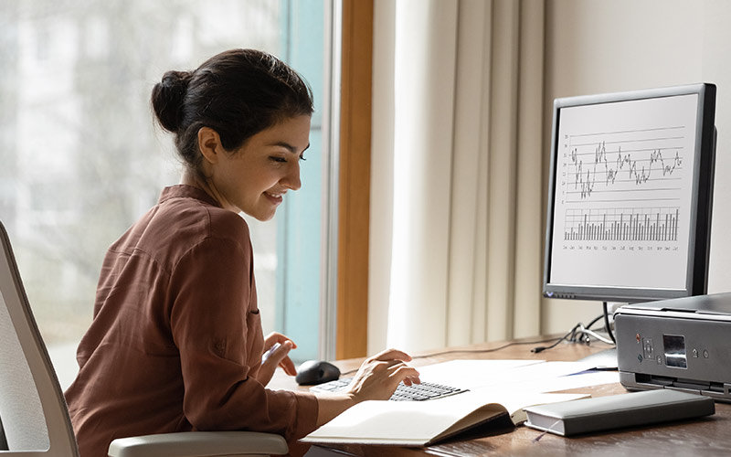 Female, with her hair pulled into a bun, in a brown blouse working on a desktop