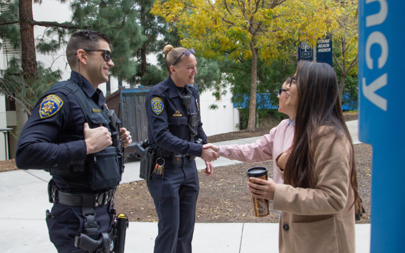 Two CSUF Police Department law enforcement officers outside near an emergency blue phone shaking the hands of two community members.