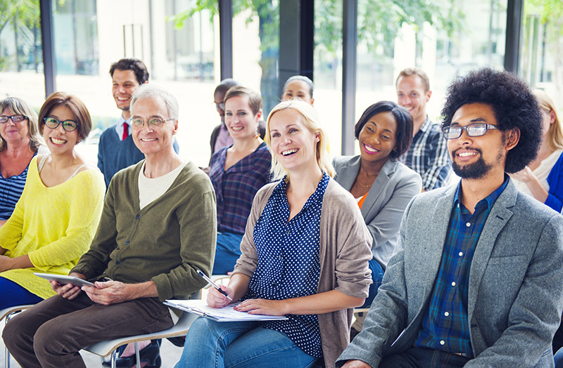 Diverse group of adults, dressed in casual or business casual attire, paying attention to a speaker