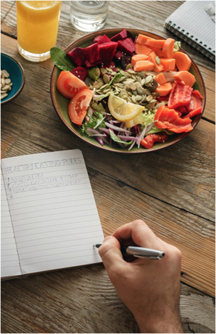 Bowl of salad, next to someone who is journaling about healthy eating
