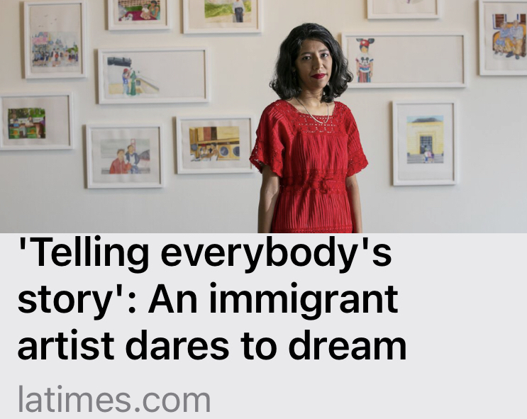 Image of artist Adriana Martinez in red dress standing in front of her framed watercolor artworks hanging upon a white wall at Grand Central Art Center