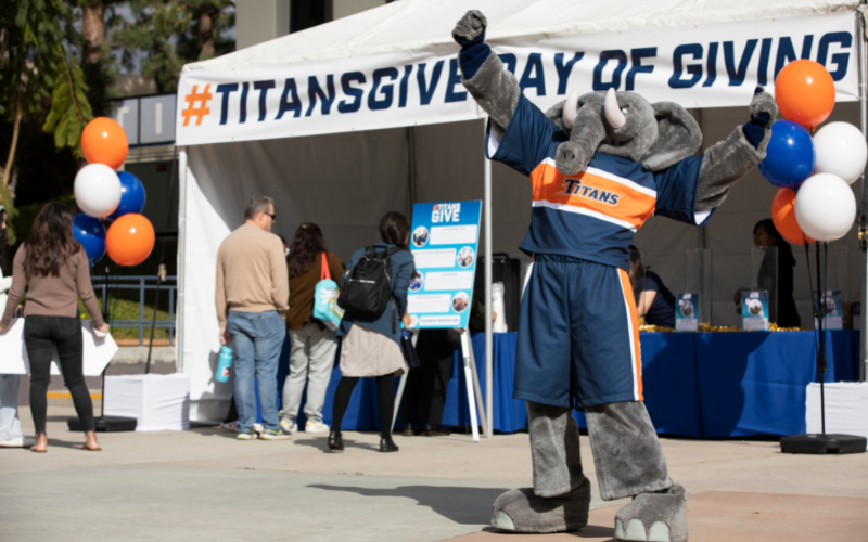 Tuffy standing in front of #TitansGive Day of Giving tent raising an arm triumphantly in the air