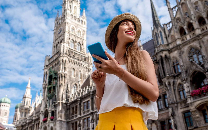 Young female holding cell phone and standing in the town hall square of Munich on a sunny day