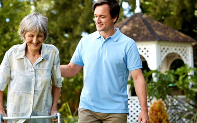 an adult male walking next to an elderly lady using a walker