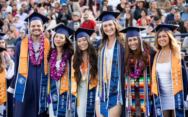 Graduating students in regalia smile and pose for photo